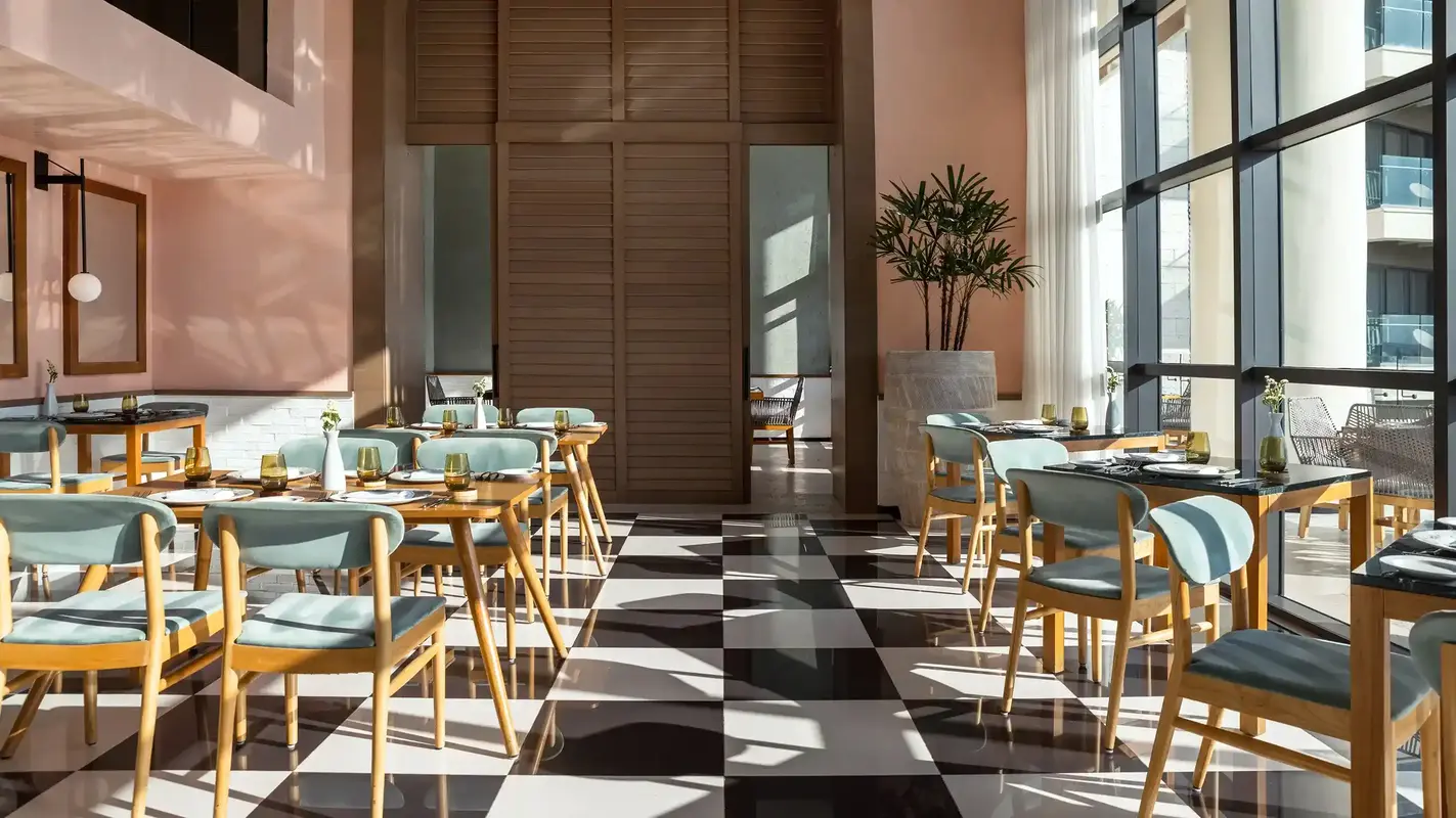 Restaurant interior with wooden tables, blue chairs, and floor-to-ceiling windows overlooking the city.