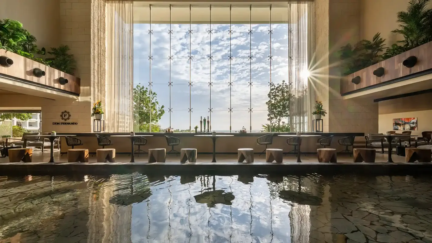 Indoor bar lounge with floor pool, large windows, seating areas, and plants.