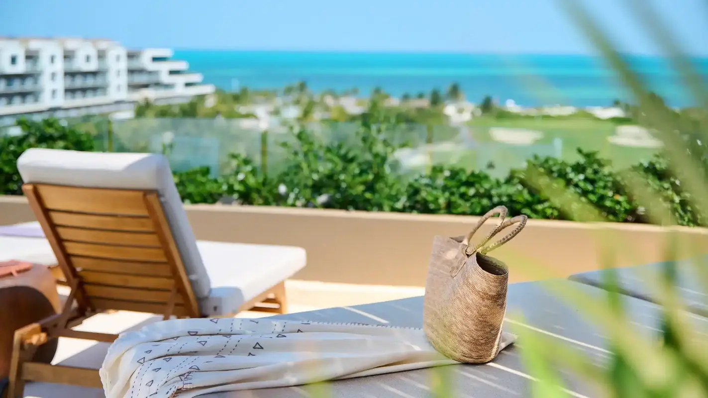 Balcony overlooking golf course, ocean, woven basket, and wooden lounge chair.