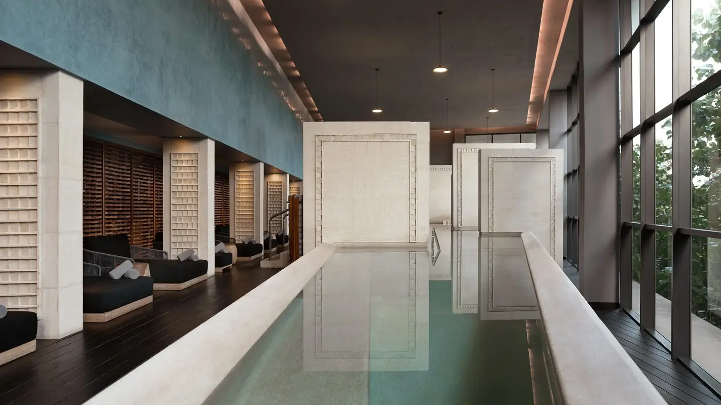 Spa relaxation area with black loungers, wooden screens, and indoor reflecting pool.